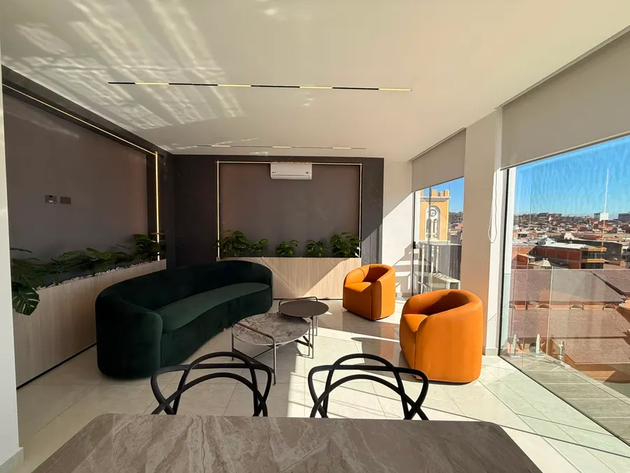 Estar del área social con sofá curvo, sillones y vista sobre la ciudad