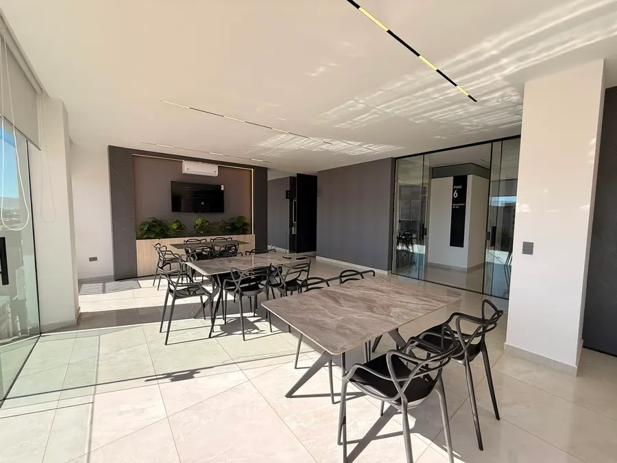 Salón del sexto piso con mesas largas, televisor y salida a la terraza