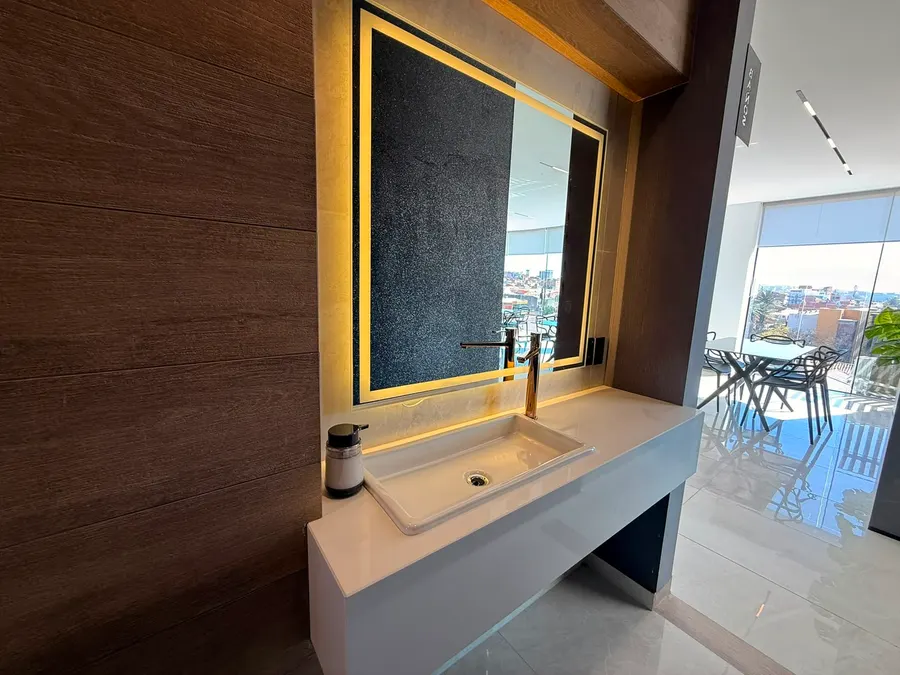 Tocador del salón con espejo retroiluminado y ventanal sobre la ciudad